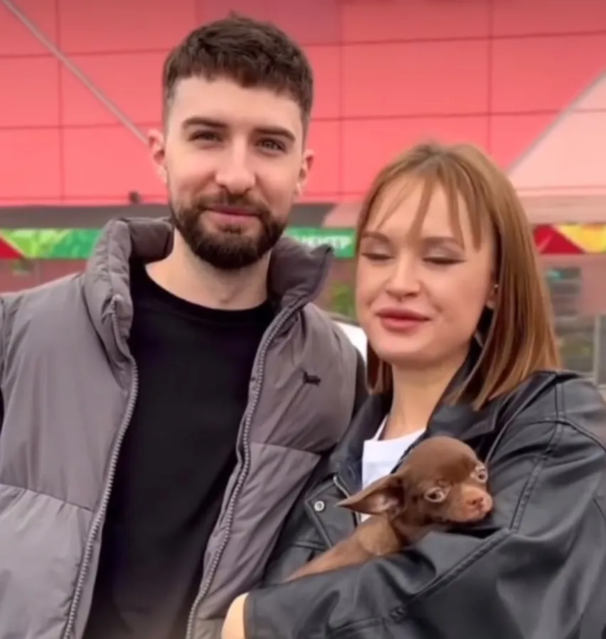 A couple holding their new chocolate chihuahua puppy on pickup day