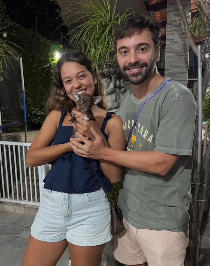 A smiling couple cradling a tiny chocolate chihuahua puppy