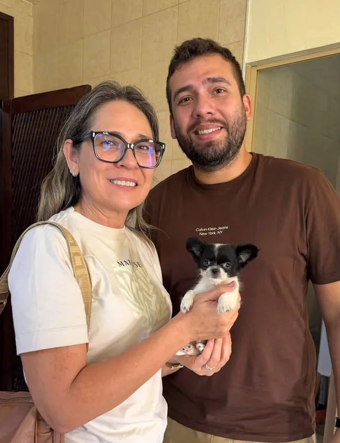 A couple holding a black and white long haired chihuahua puppy