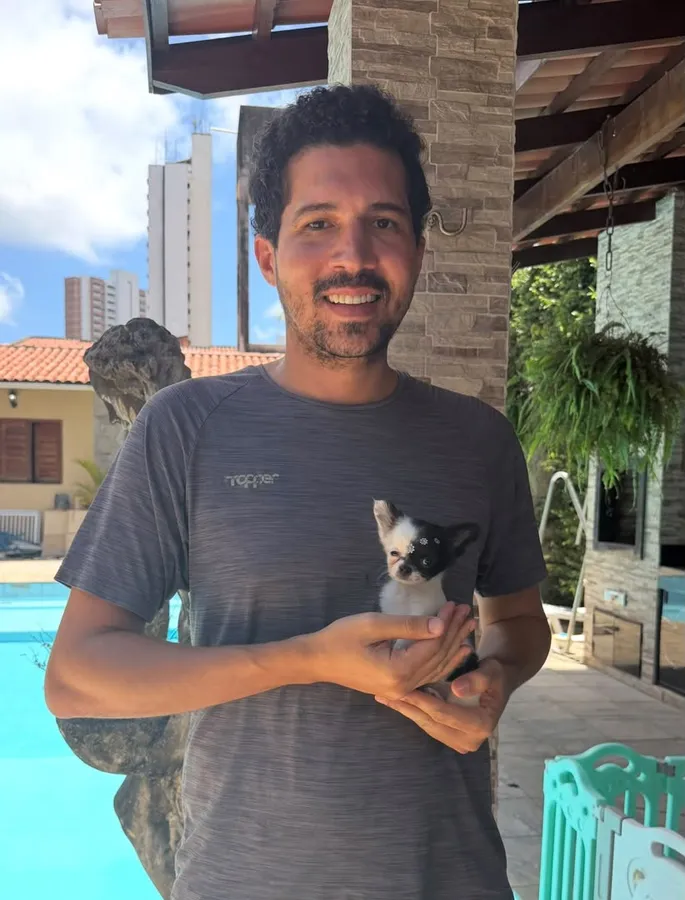 A man holding a small black and white chihuahua puppy