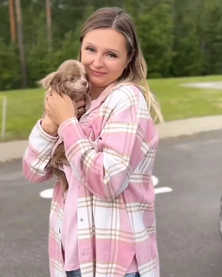A woman in a pink shirt holding a chocolate long haired chihuahua puppy