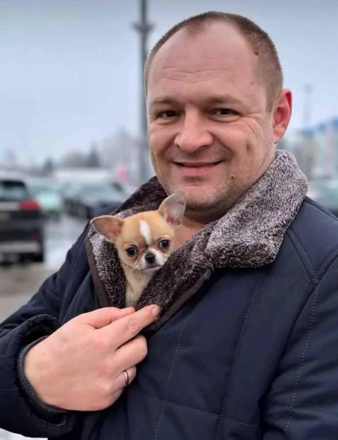 A man carrying a fawn chihuahua puppy tucked into his coat